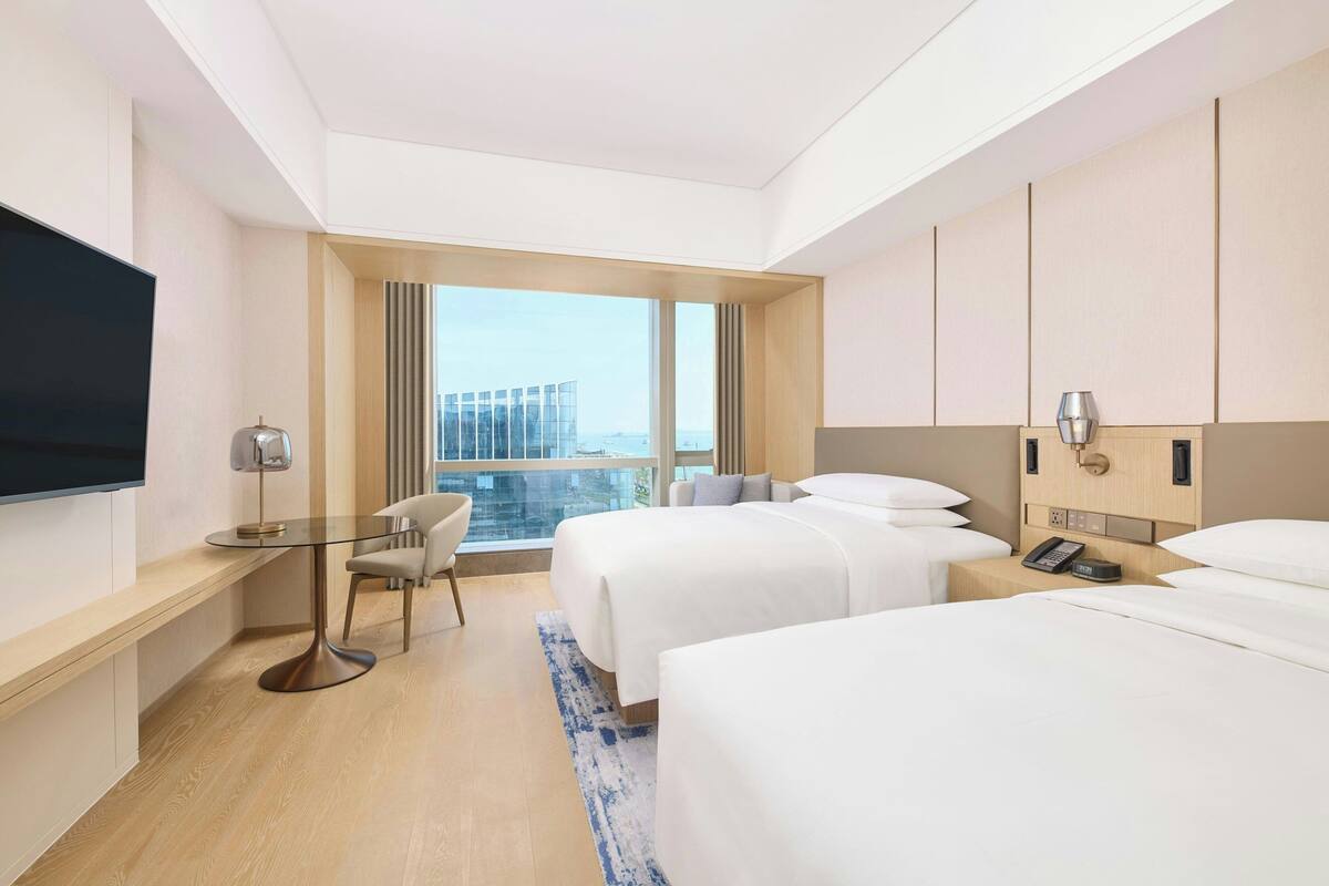 Une chambre d’hôtel avec deux lits, un bureau avec une chaise, une télévision et une grande fenêtre donnant sur la ville.