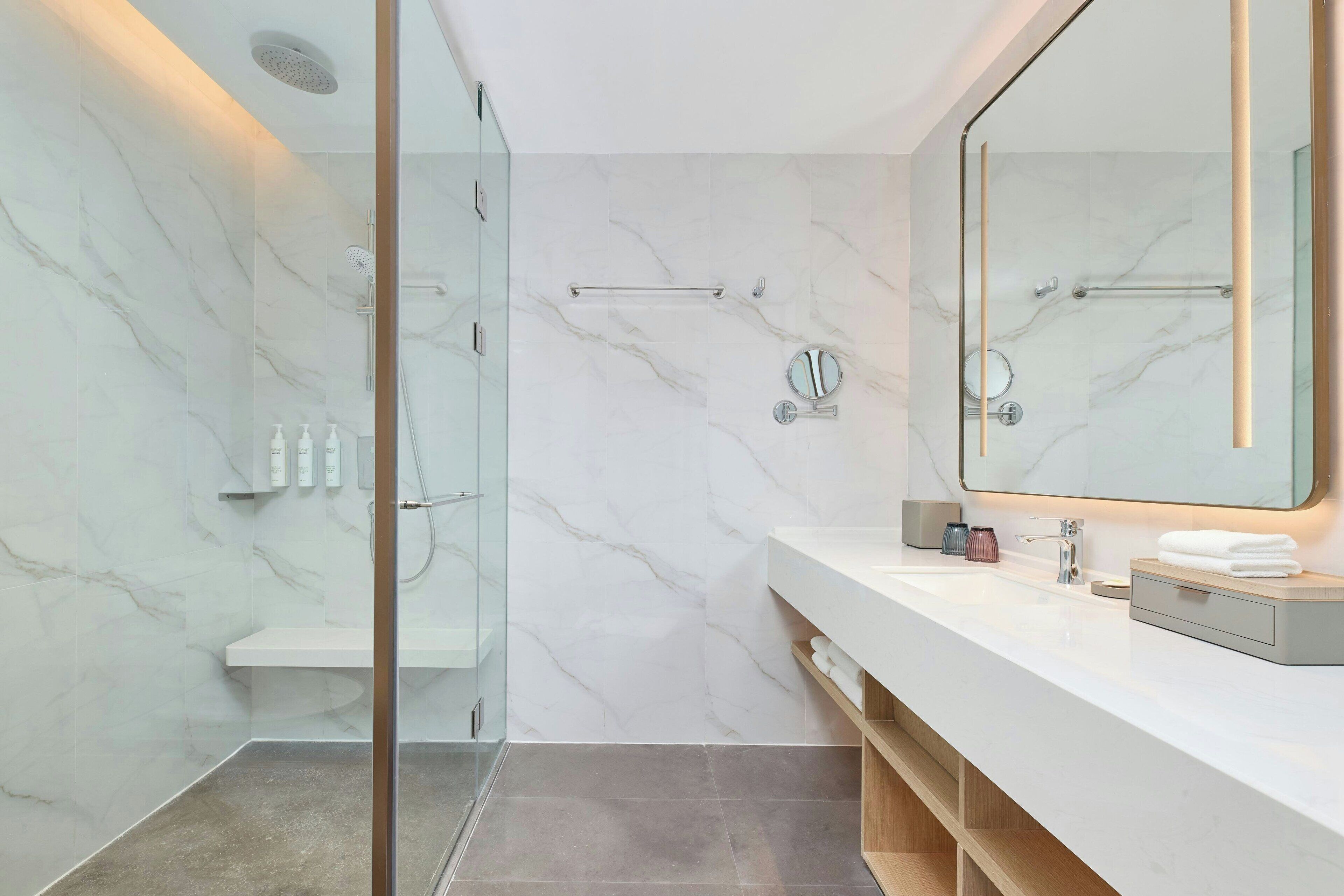 Une salle de bain moderne avec une douche à parois de verre, un grand miroir et un meuble-lavabo blanc doté d’un porte-serviettes.