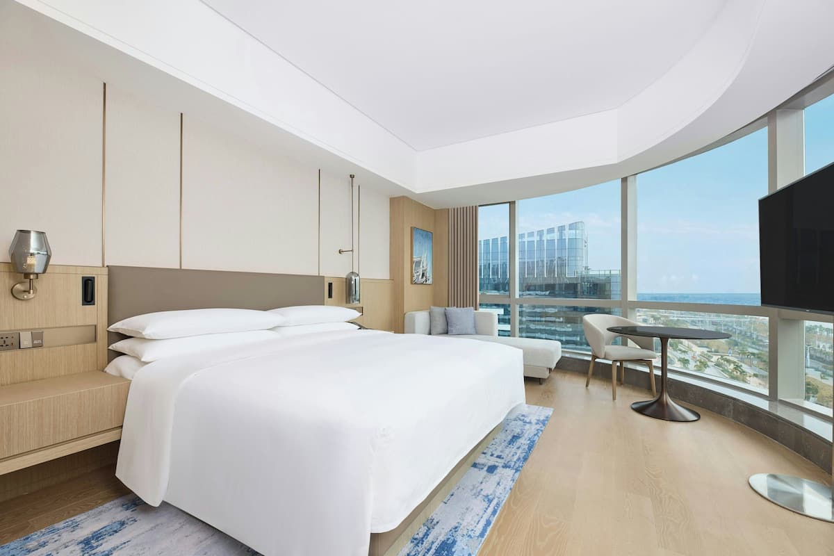 Une chambre d’hôtel moderne dotée d’un grand lit, d’un coin salon, d’une télévision et offrant une vue sur la ville.