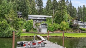 Une jetée avec un bateau et des chaises, une petite cabane et un bâtiment entouré d’arbres.