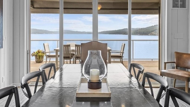 Un coin repas avec une table et des chaises, un centre de table décoré de bougies et une vue sur un lac, visible à travers de grandes fenêtres.