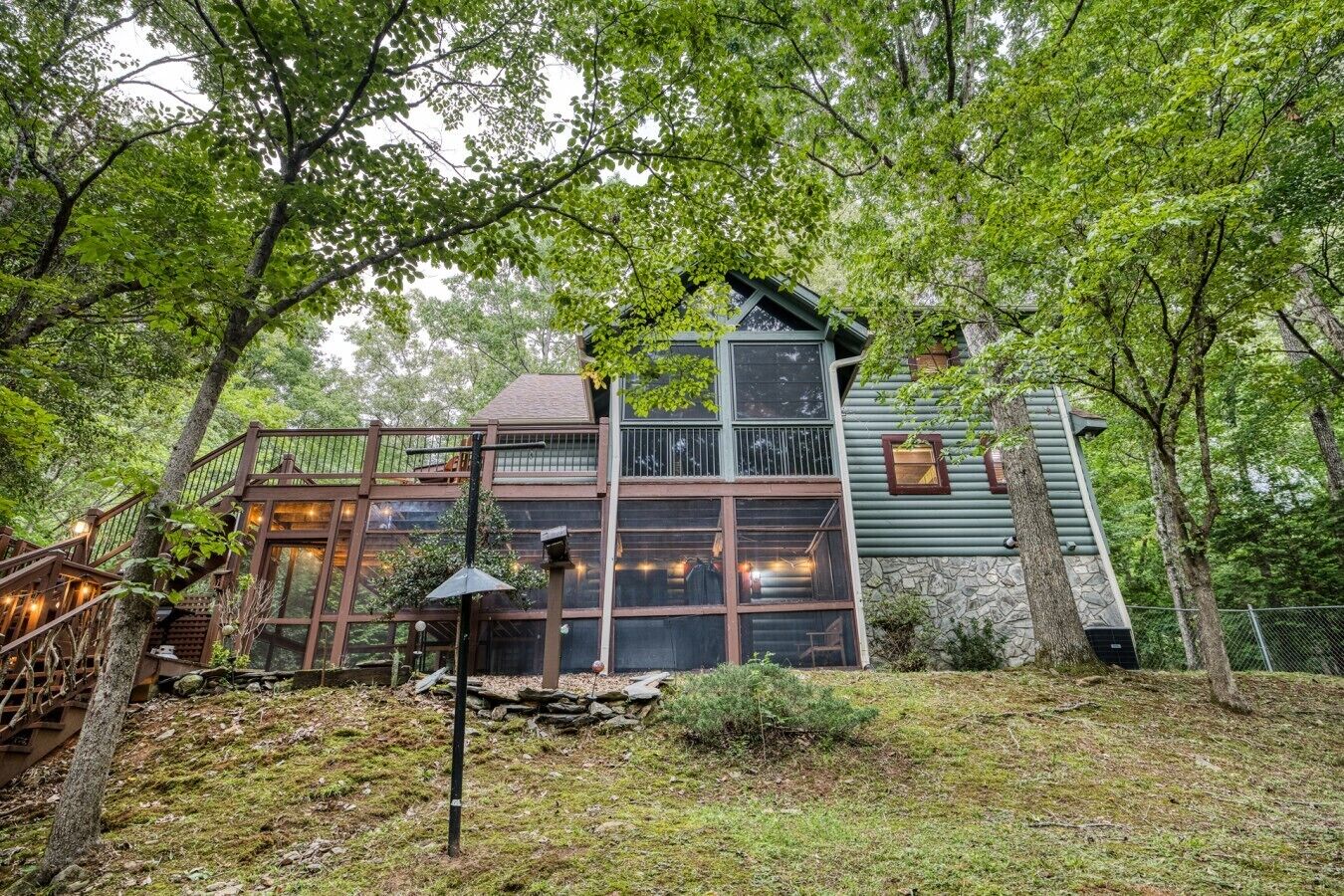 A cabin with a wooden deck, large windows, and a stone foundation.