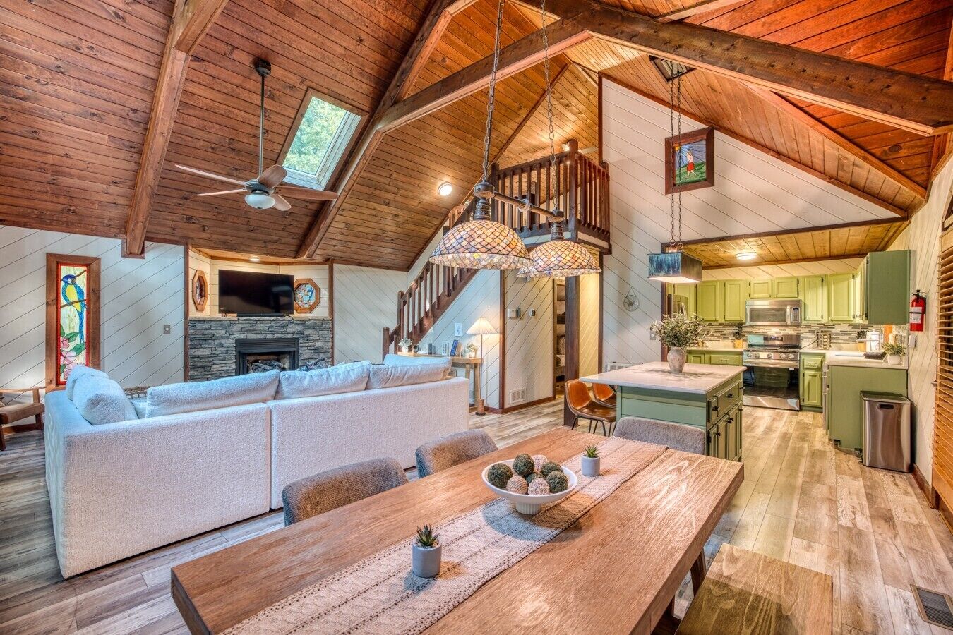 A spacious loft with a high ceiling, a dining area with a wooden table, a built-in kitchen, and a cozy seating area with a fireplace.