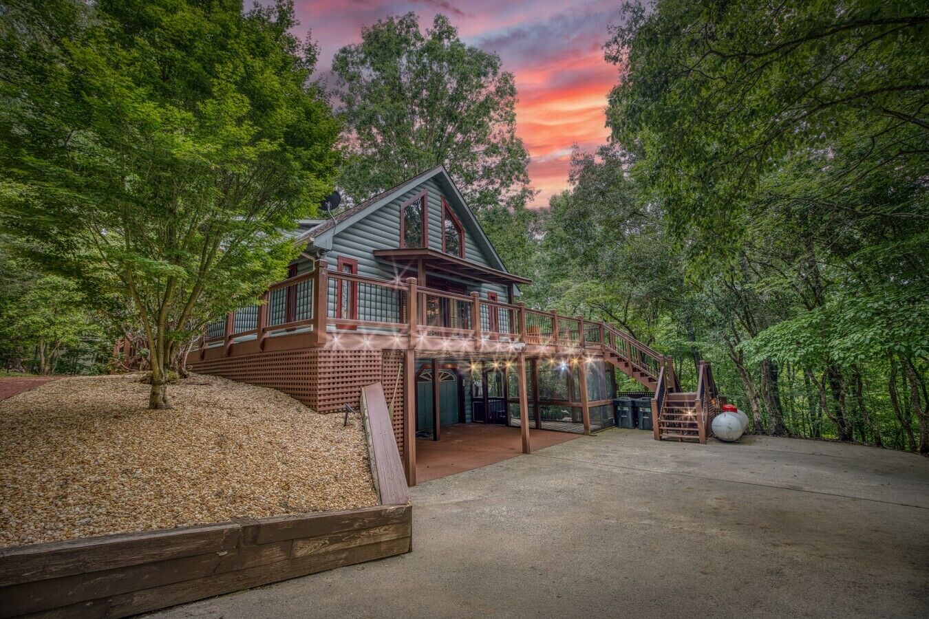 A cabin with a wooden deck, surrounded by trees, and a clear sky.