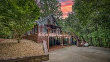A cabin with a wooden deck, surrounded by trees, and a clear sky.