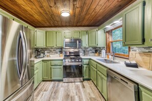 A kitchen with green cabinets, stainless steel appliances, and a wooden ceiling. - Starling Hollow • Hot Tub | Fire Pit | Family Vibe (Blue Ridge)