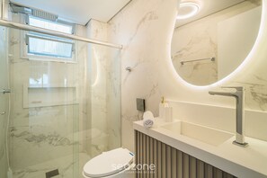 A modern bathroom with a glass shower enclosure, a white sink with a marble countertop, and a large mirror with a curved frame. - Full apt Near Ufsc in Florianopolis Cec0612 (Florianópolis)