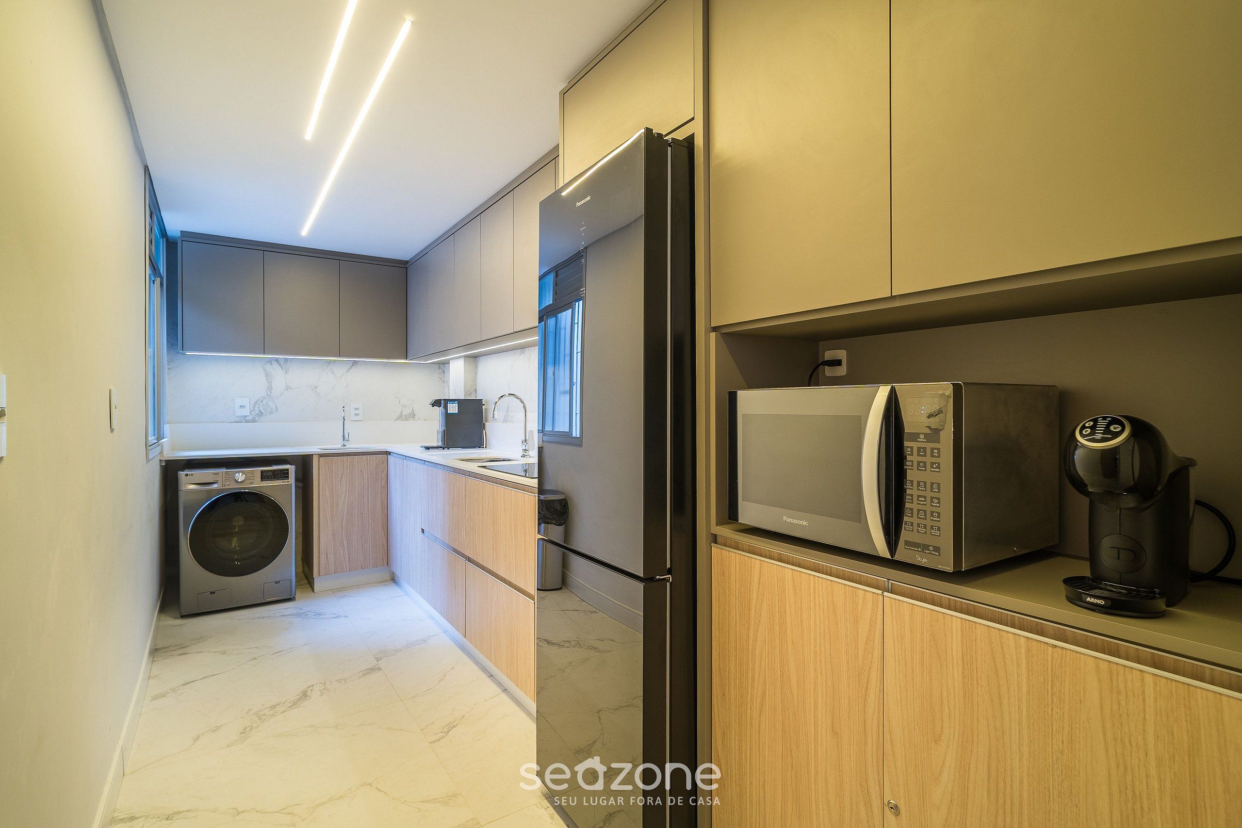 A modern kitchen with a washing machine, refrigerator, microwave, and coffee maker.