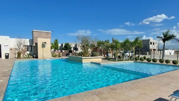 A swimming pool with clear blue water, surrounded by a paved area with a few palm trees and a building in the background. - 3 Bedroom House In Secure Privada (La Paz)