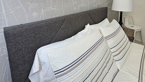 Une chambre d’hôtel comprenant un lit, une tête de lit, une table de chevet, une lampe et un mur recouvert d’un papier peint sur le thème de la marine.