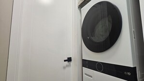 Une buanderie équipée de deux machines à laver à chargement frontal superposées et d’une porte blanche.