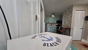 Une cuisine avec des meubles de couleur bleu clair, un mur en bois et un plan de travail blanc orné d’un motif sur le thème de la plage.
