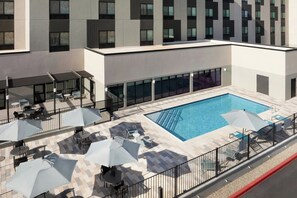 A rooftop pool area with lounge chairs and umbrellas, surrounded by a building with large windows. - Towneplace Suites By Marriott Casa Grande (Casa Grande)