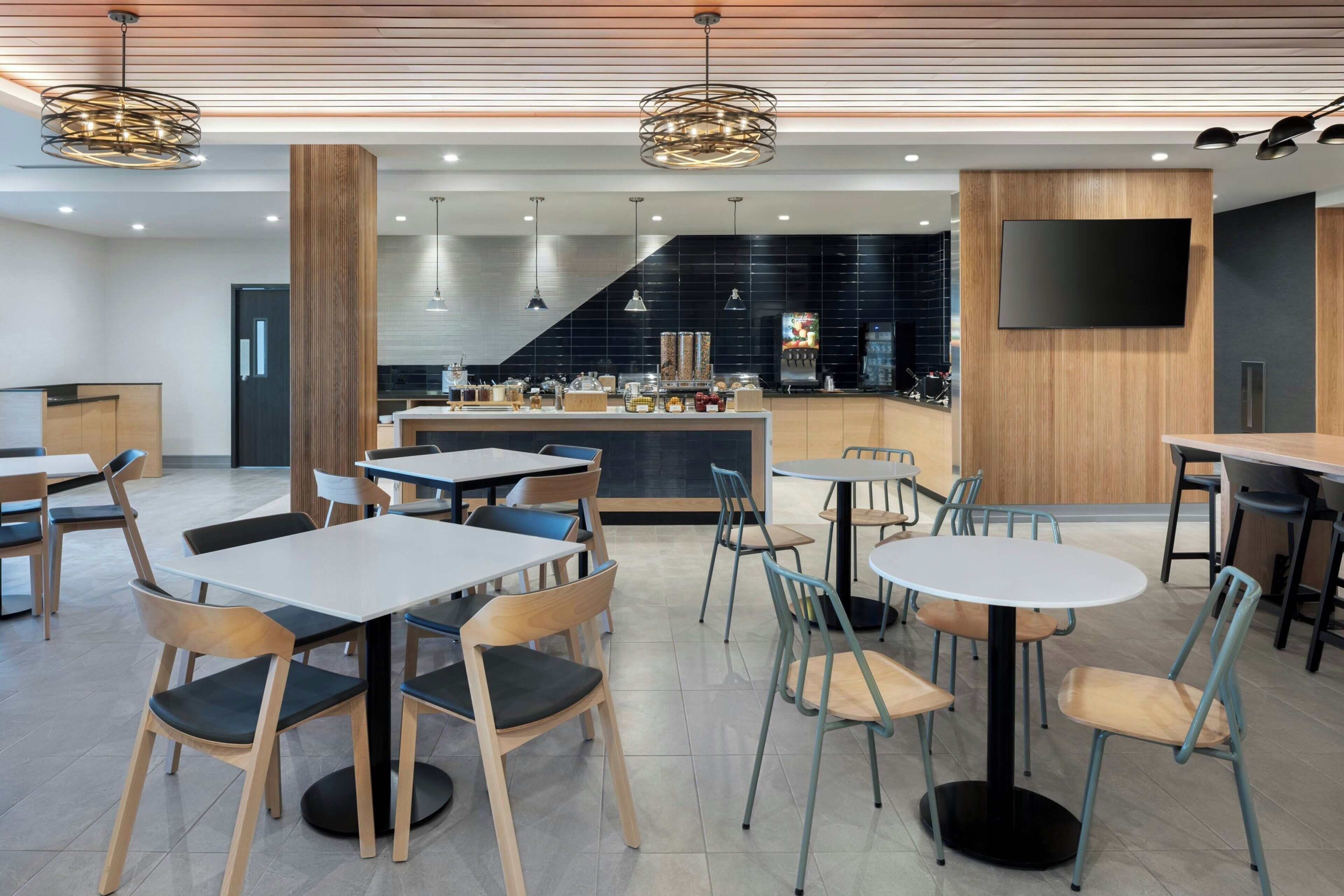 A modern restaurant with multiple seating areas, including tables and chairs, a bar area with a coffee machine, and a flat-screen TV mounted on the wall.