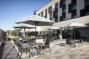 An outdoor patio area with tables and chairs, umbrellas, and a building in the background. - Towneplace Suites By Marriott Casa Grande (Casa Grande)