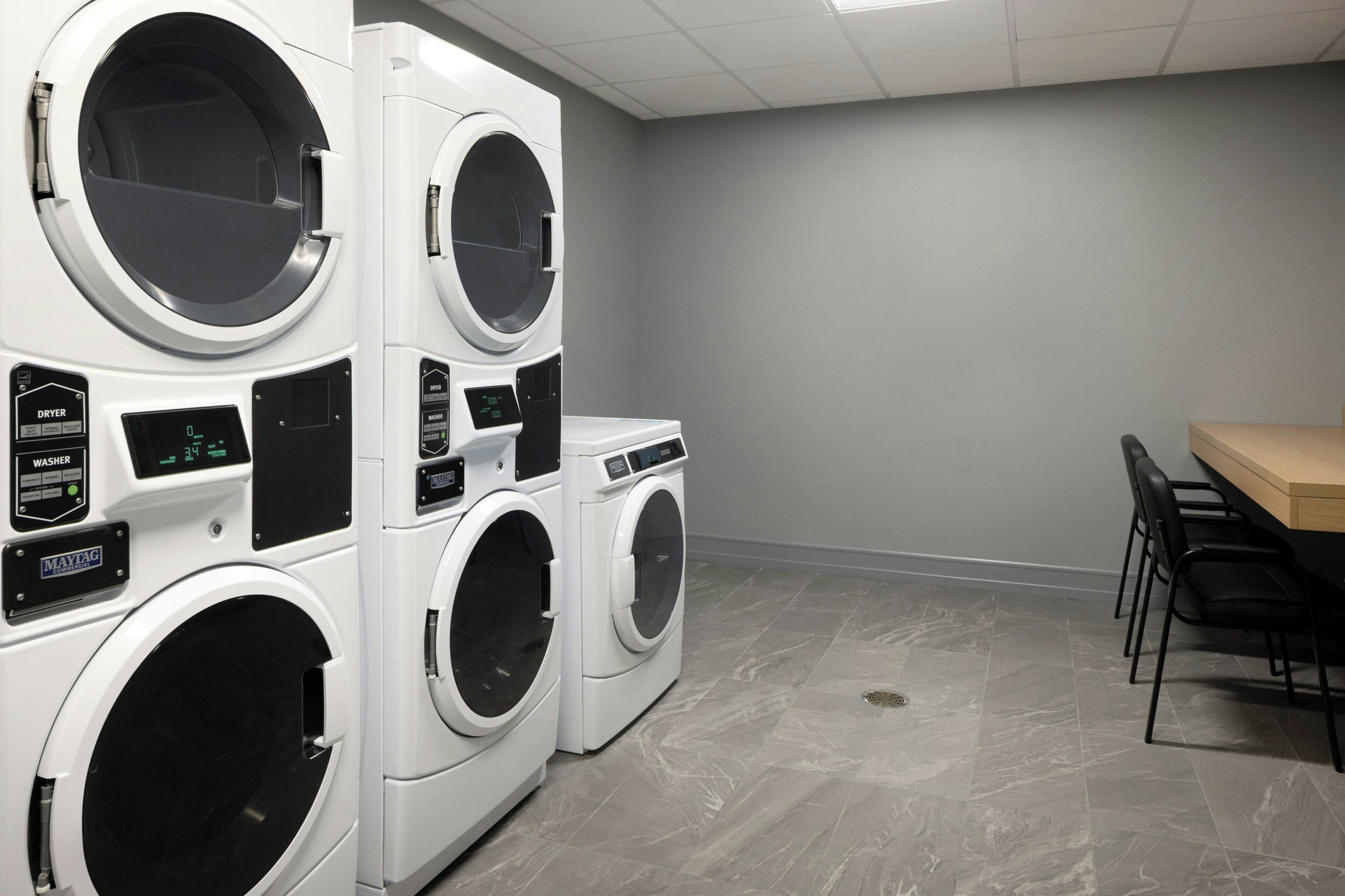 A laundry room with multiple washing machines and dryers, a table, and chairs.