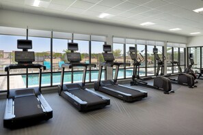 Un gimnasio con cintas de correr, bicicletas estáticas y vista a la piscina.