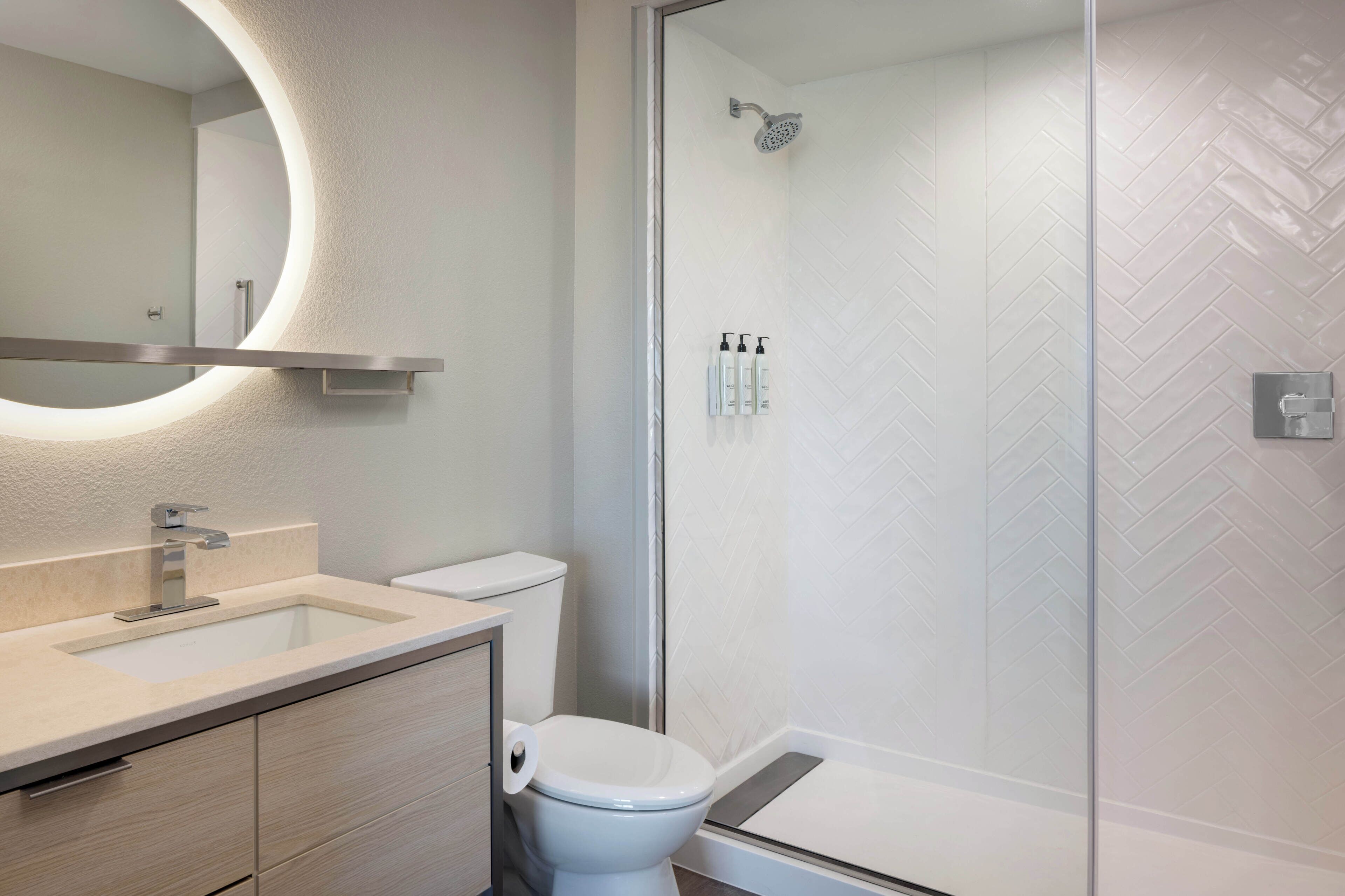 A modern bathroom with a glass-enclosed shower, a round mirror, and a toilet.