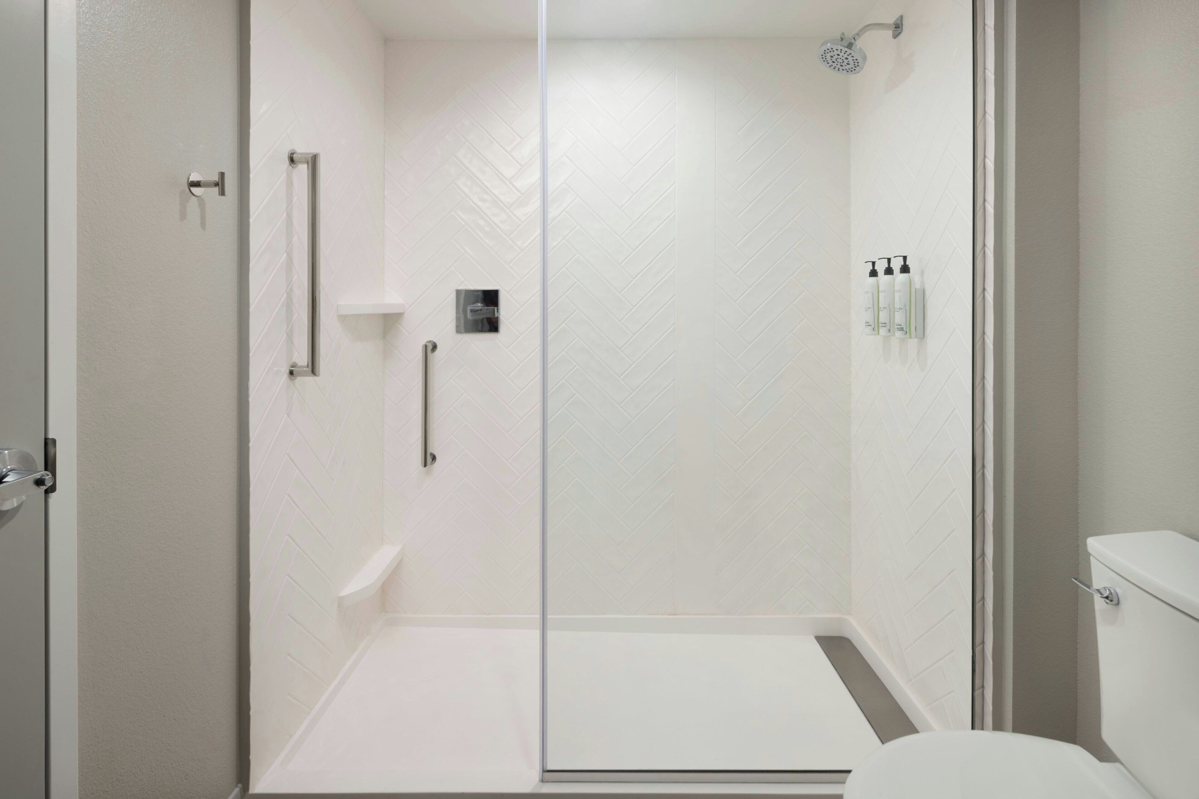 A modern bathroom with a glass shower enclosure, a toilet, and a shelf with toiletries.
