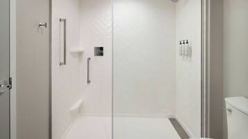 A modern bathroom with a glass shower enclosure, a toilet, and a shelf with toiletries.