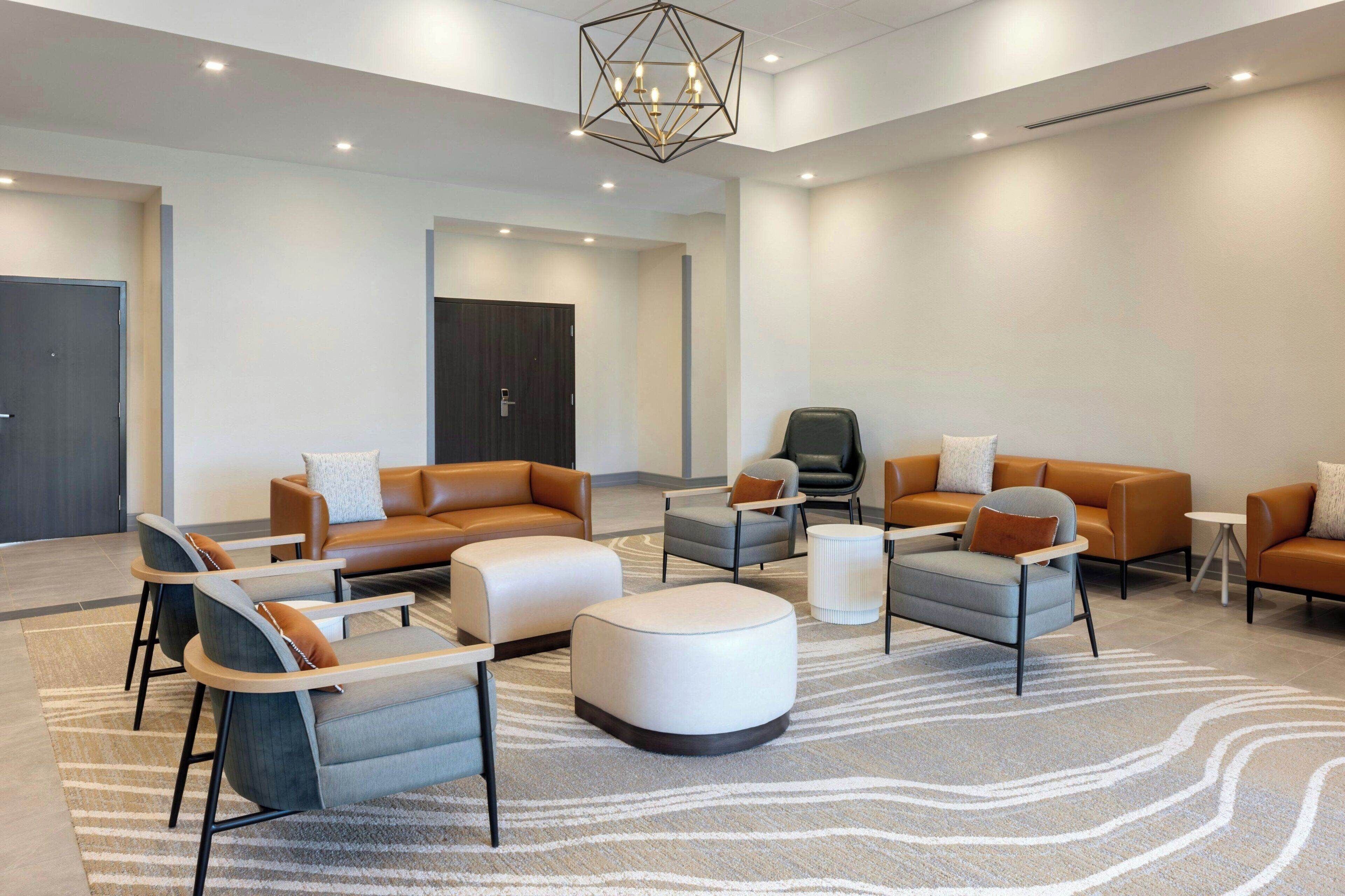 A modern hotel lobby with leather sofas, armchairs, and a central ottoman.