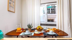Aamiaispöydällä on kulho täynnä hedelmiä, croissantteja ja lasi appelsiinimehua.