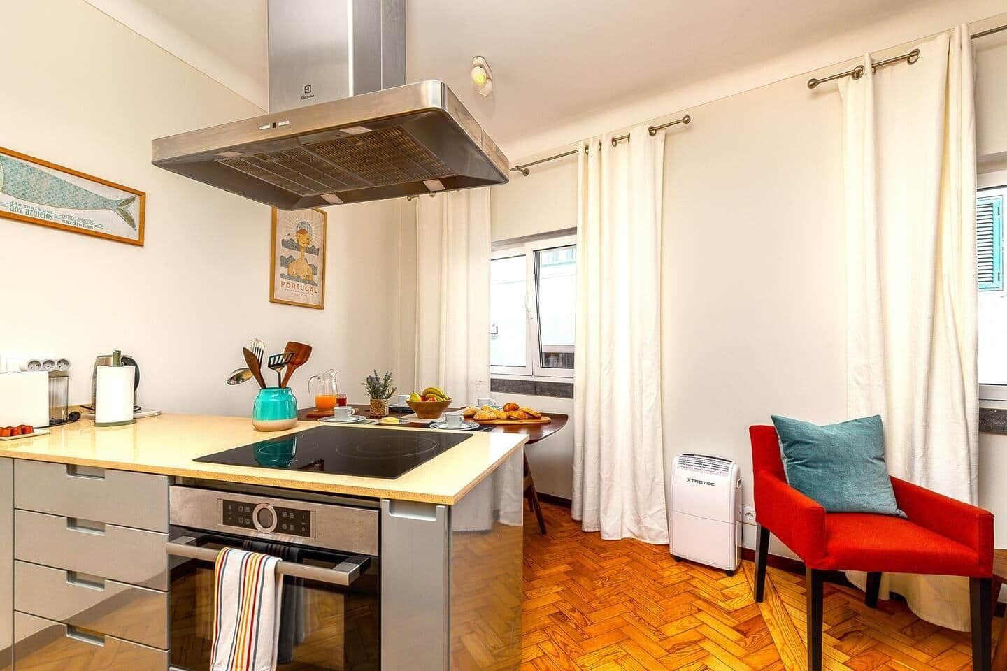 A compact kitchen with a central island, a built-in oven, and a window with curtains.