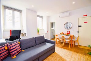 Ein modernes Wohnzimmer mit grauem Sofa, einem Esstisch mit Stühlen und einer kleinen Küchenzeile.