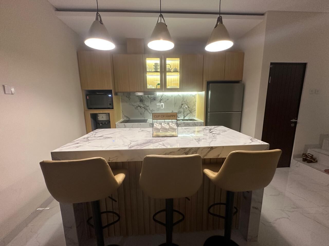 A modern kitchen with a marble island, three bar stools, pendant lighting, and wooden cabinets.
