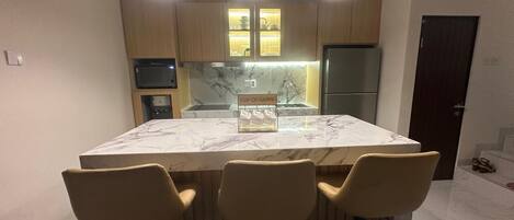 A modern kitchen with a marble island, three bar stools, pendant lighting, and wooden cabinets.
