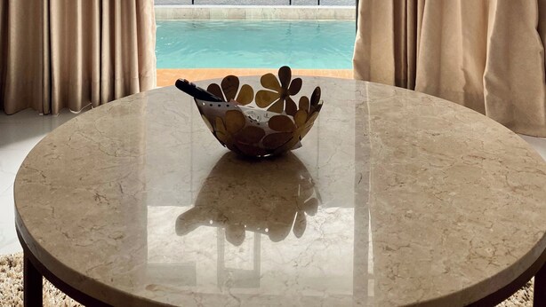 A room with a marble table, a decorative bowl, and a view of a swimming pool through beige curtains. - Luxury central Denpasar home with pool and clubhouse for an easy family stay. (Denpasar Barat)