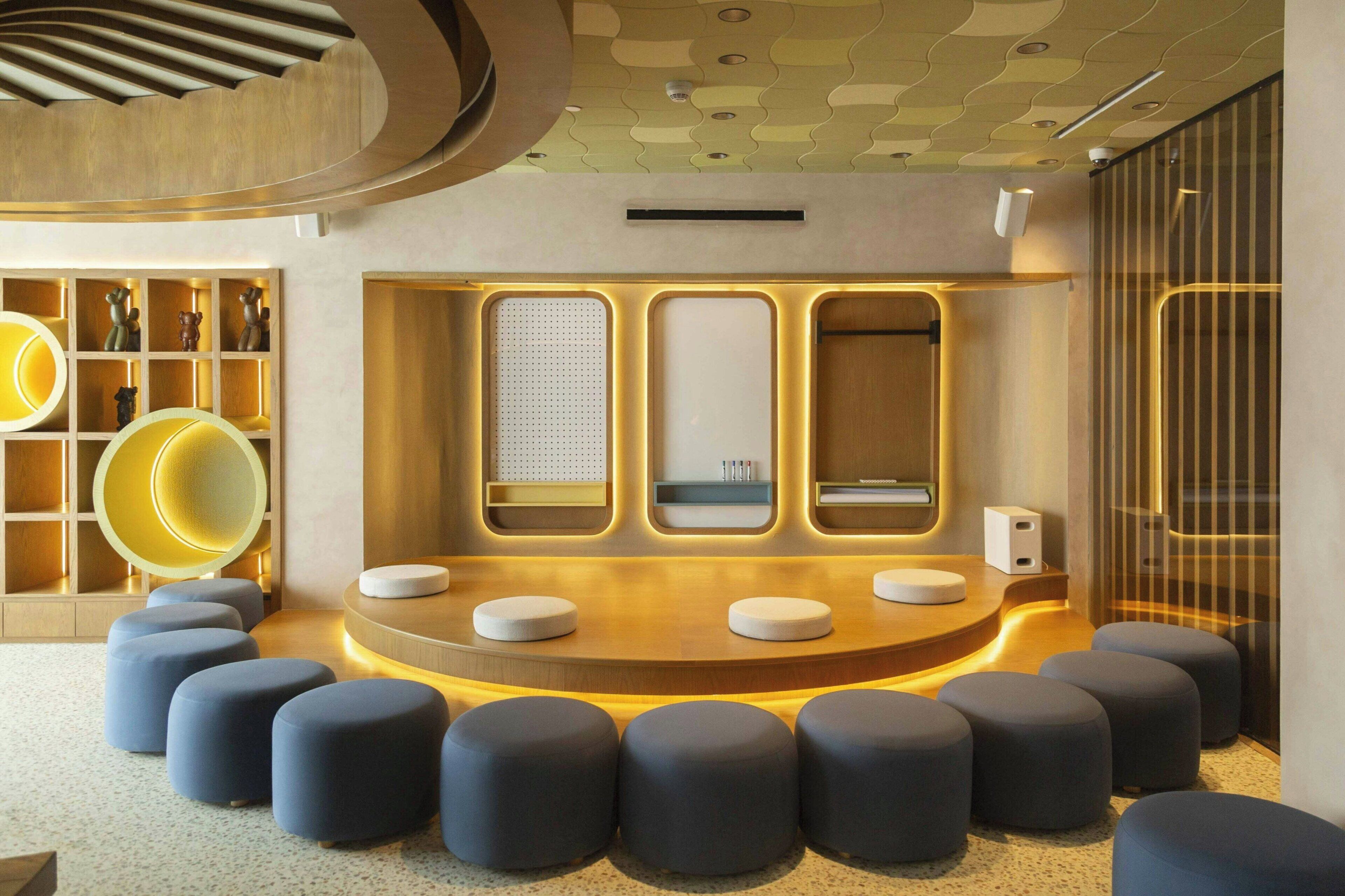 A modern interior with a central seating area, a wooden reception desk, and a patterned ceiling.