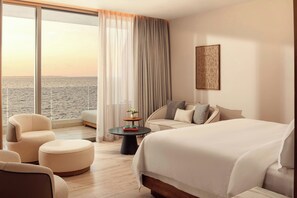 Une chambre d’hôtel avec un grand lit, un canapé, un fauteuil, une petite table et une vue sur la mer.