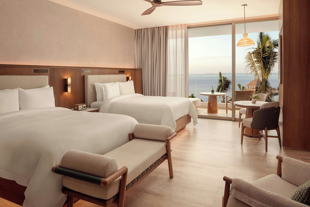 A hotel room with two beds, a sitting area with a view, and a balcony with a table and chairs.