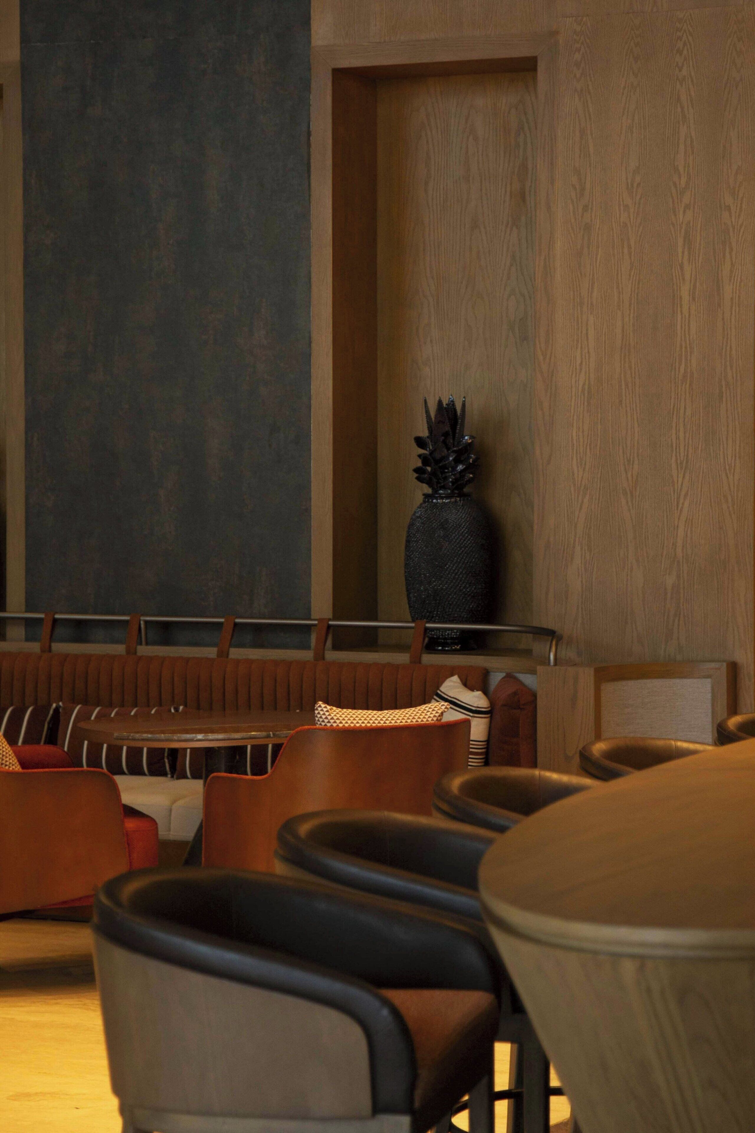 A seating area with a mix of chairs and a bench, a large vase with a plant, and a wall with a textured pattern.