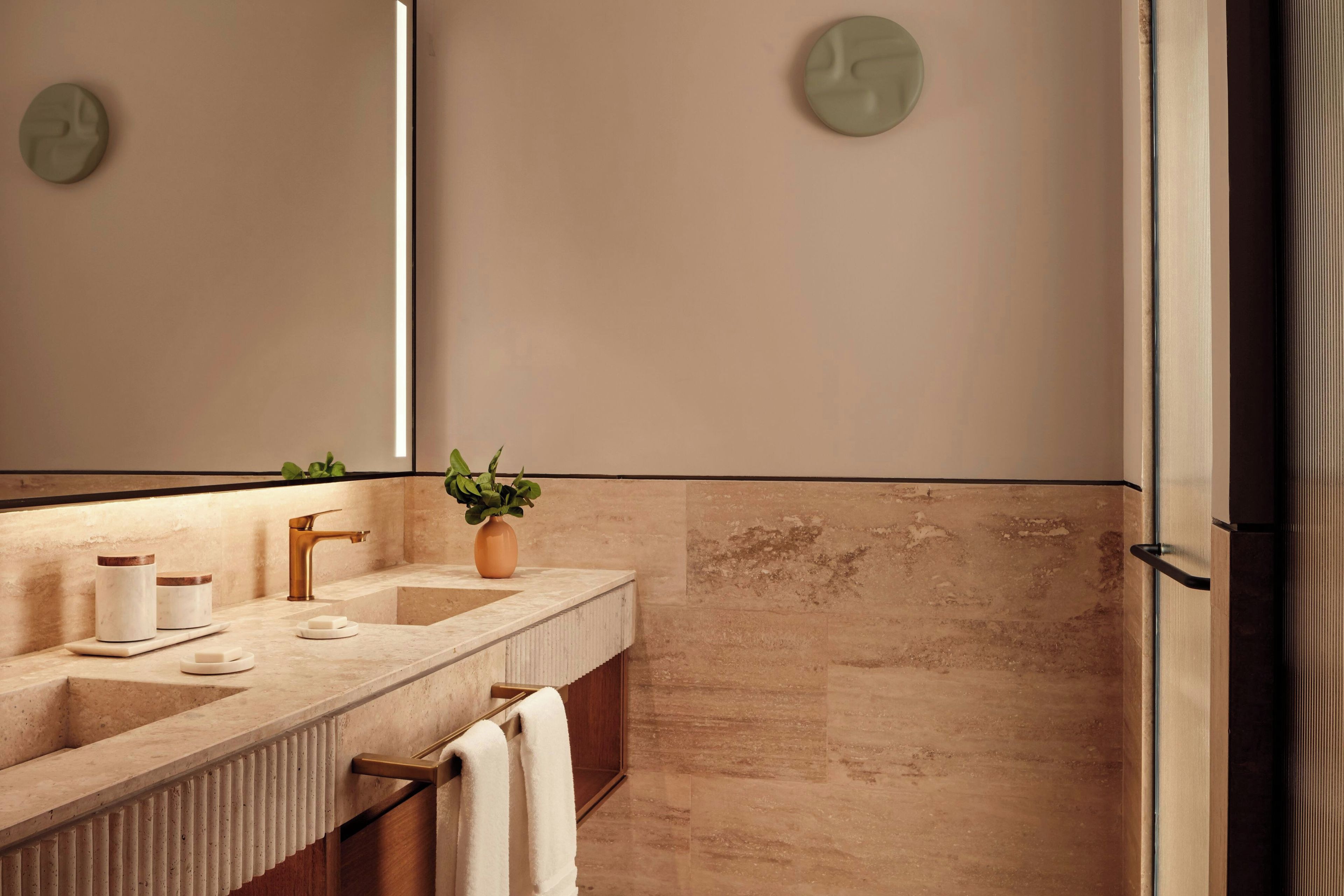 Ein Badezimmer mit Marmorwaschbecken, goldenem Wasserhahn, einer Topfpflanze und einem Handtuchhalter.