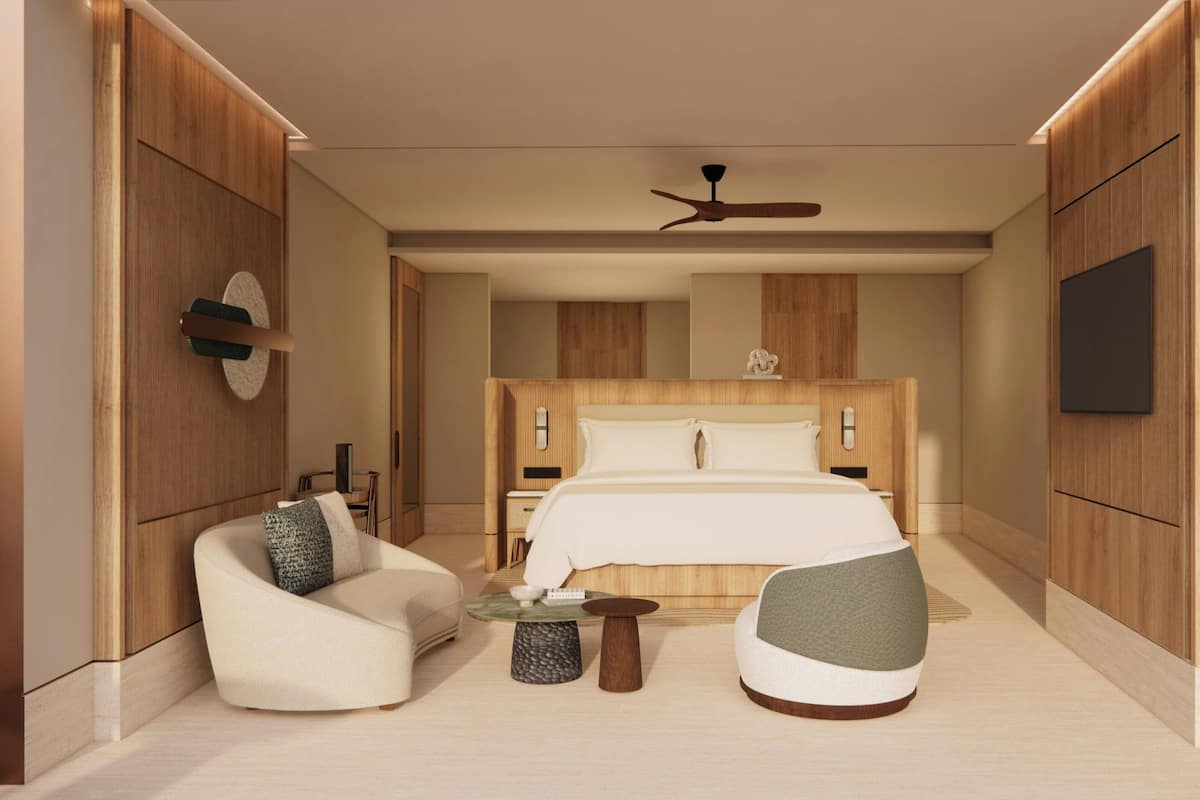 A modern hotel room with a large bed, a ceiling fan, a TV, and a seating area with two chairs and a small table.