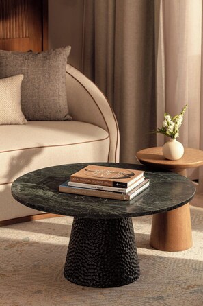 A modern living room with a round black coffee table, a beige sofa, and a small wooden side table with a vase of flowers. - The St. Regis Costa Mujeres Resort, Cancun (Cancun)