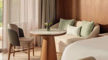 Habitación de hotel con cama, sofá, sillón, una mesa redonda de madera y una lámpara colgante.