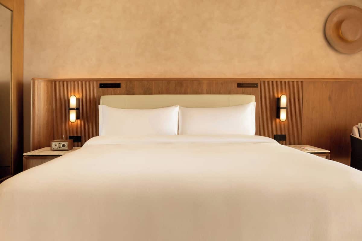 A large bed with a wooden headboard, two bedside tables with lamps, and a wall-mounted hat.