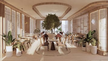 A spacious lobby with a central round table, surrounded by seating, and a large tree.