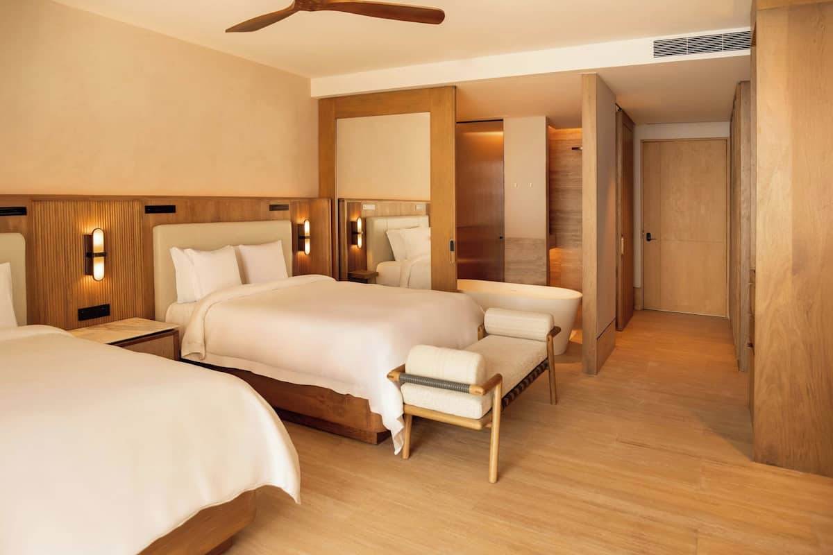 A hotel room with a large bed, bedside tables, a chair, a ceiling fan, and a wooden floor.