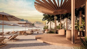 Un área de descanso frente a la playa, con tumbonas, sombrillas y una terraza de madera con vista al océano.