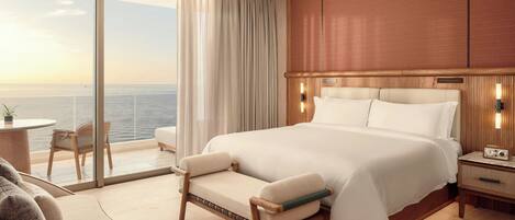 A hotel room with a large bed, a sitting area with a chair, a small table, and a view of the ocean.