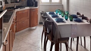A kitchen with wooden cabinets, a stove, and a dining table set with blue plates and green glassware. - Your Authentic Retreat in the Heart of Naples. (Napoli)