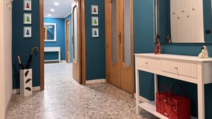 A hallway with a blue wall, wooden doors, a white console table with a red bag, and a mirror above it. - Your Authentic Retreat in the Heart of Naples. (Napoli)