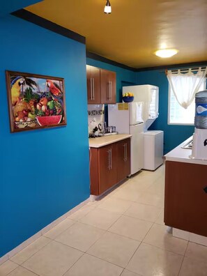 A kitchen with blue walls, wooden cabinets, a white refrigerator, and a water dispenser. - Vibrant 2BD Downtown Cozumel Condo • Walk to Shops, Dining & Ferry (Cozumel)