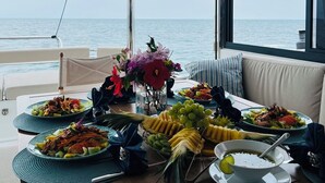 Een eettafel met verschillende gerechten en fruit, op een boot met uitzicht op zee.