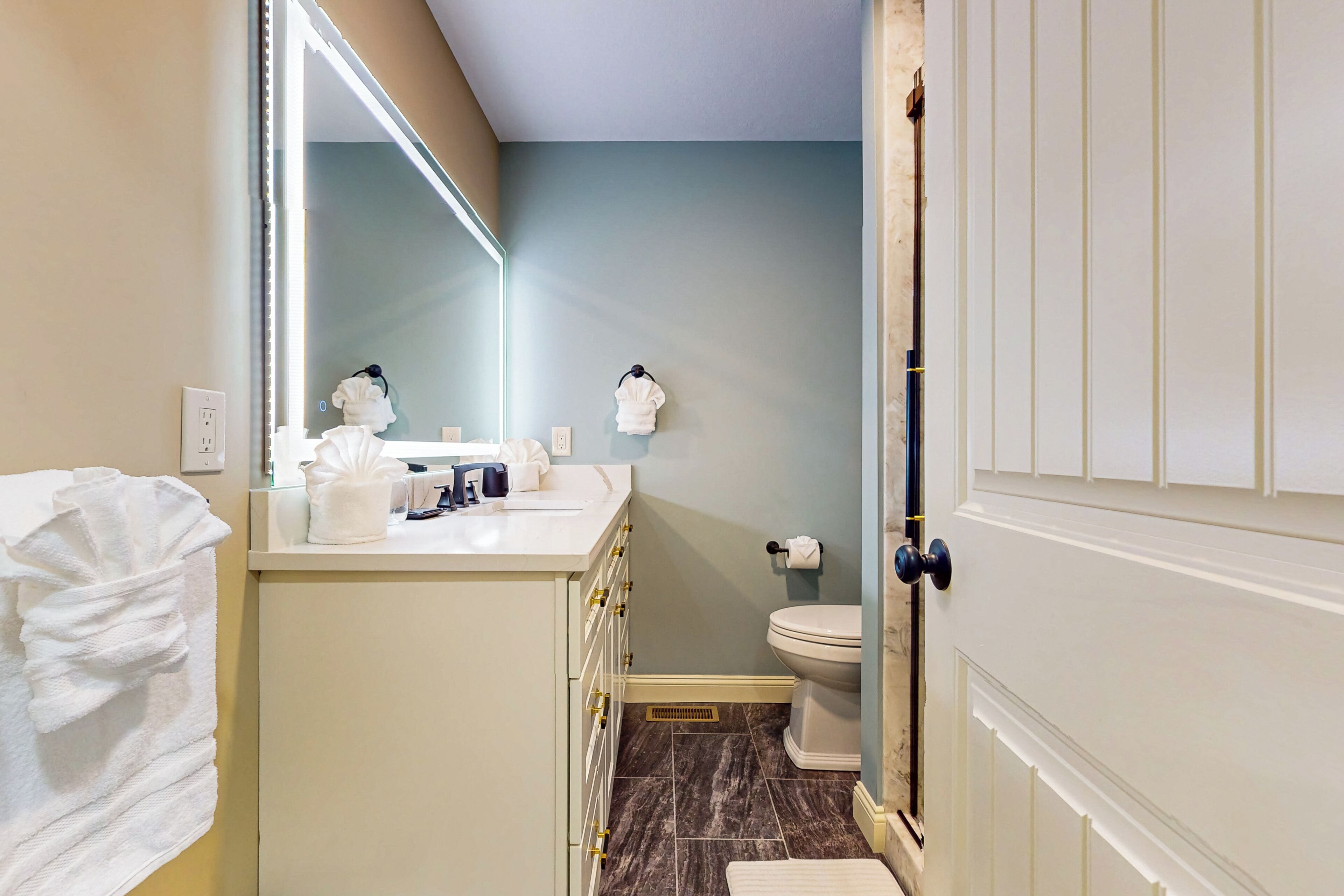 A bathroom with a white vanity, a mirror, a towel rack, a toilet, and a door with a handle.