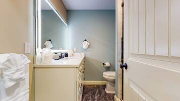 A bathroom with a white vanity, a mirror, a towel rack, a toilet, and a door with a handle.